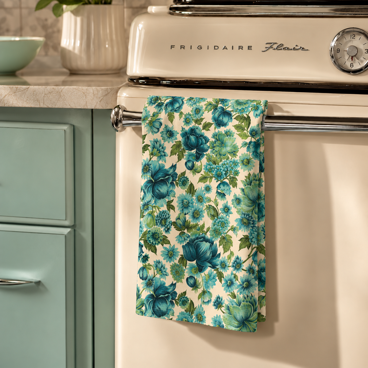 Floral kitchen towel hanging on oven handle, teal and green blossom pattern